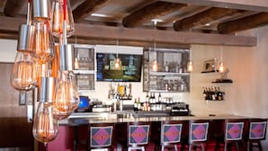 A bar area with hanging light fixtures, a television, and bar stools with patterned cushions. - The Sage Hotel (Santa Fe)