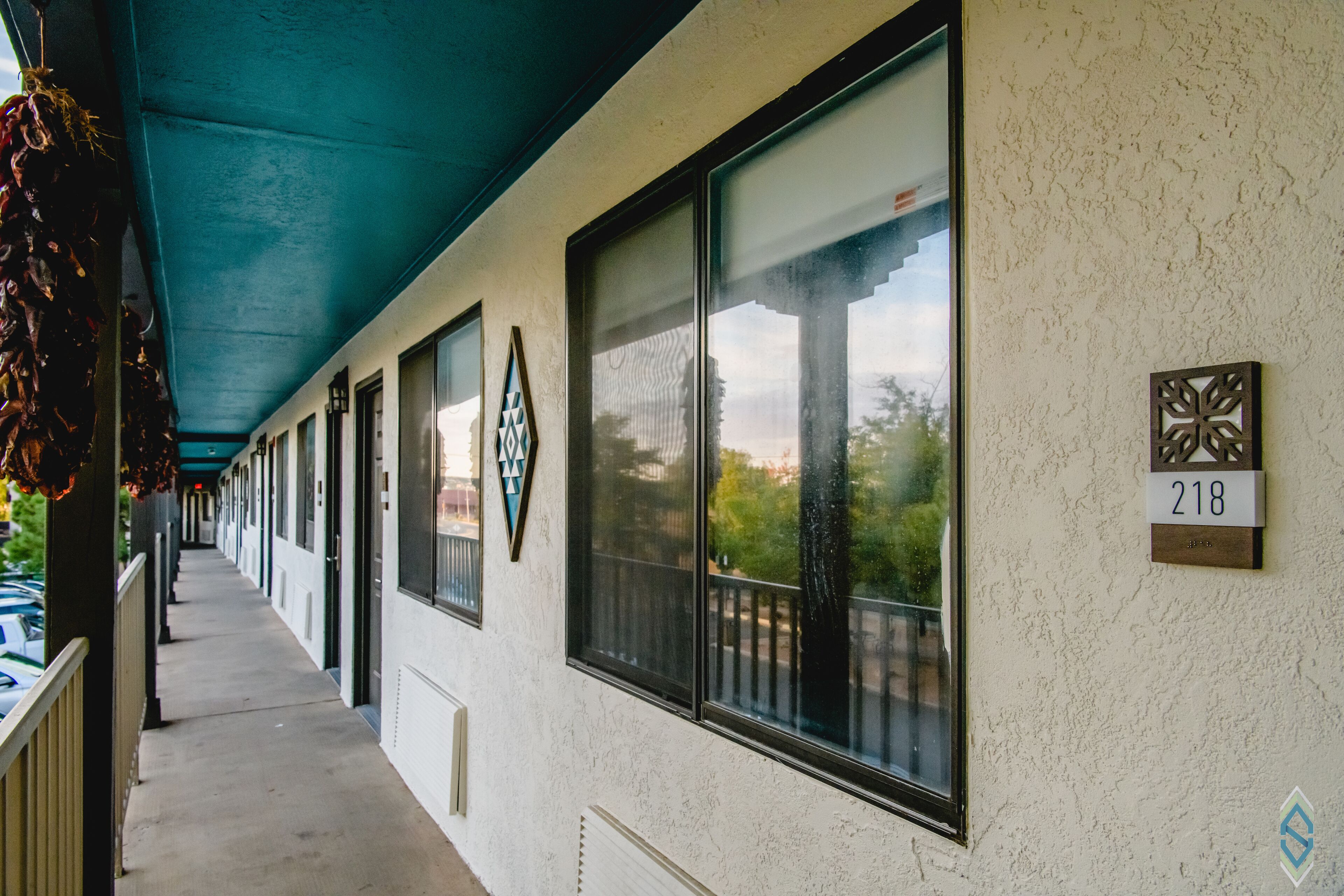 A covered corridor with large windows, a number sign '218', and a decorative wall piece.