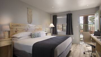 A modern hotel room with a large bed, a desk with a computer, a chair, and a view of the outdoors.