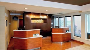 Un área de recepción con dos mostradores de madera, un televisor montado y grandes ventanales con vistas al exterior.