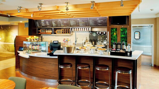Un área de bar moderna con mostrador de madera, taburetes y una pizarra de menú.