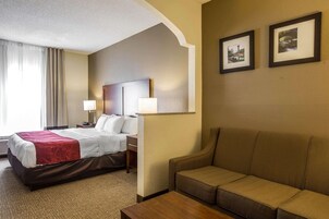 Una habitación de hotel con cama, sofá, escritorio, dos lámparas y dos cuadros en la pared.