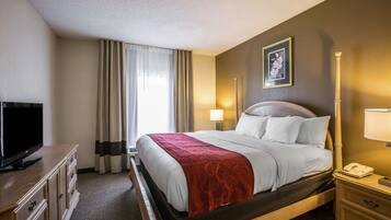 A hotel room with a bed, a TV, a bedside table, a lamp, and a picture on the wall.