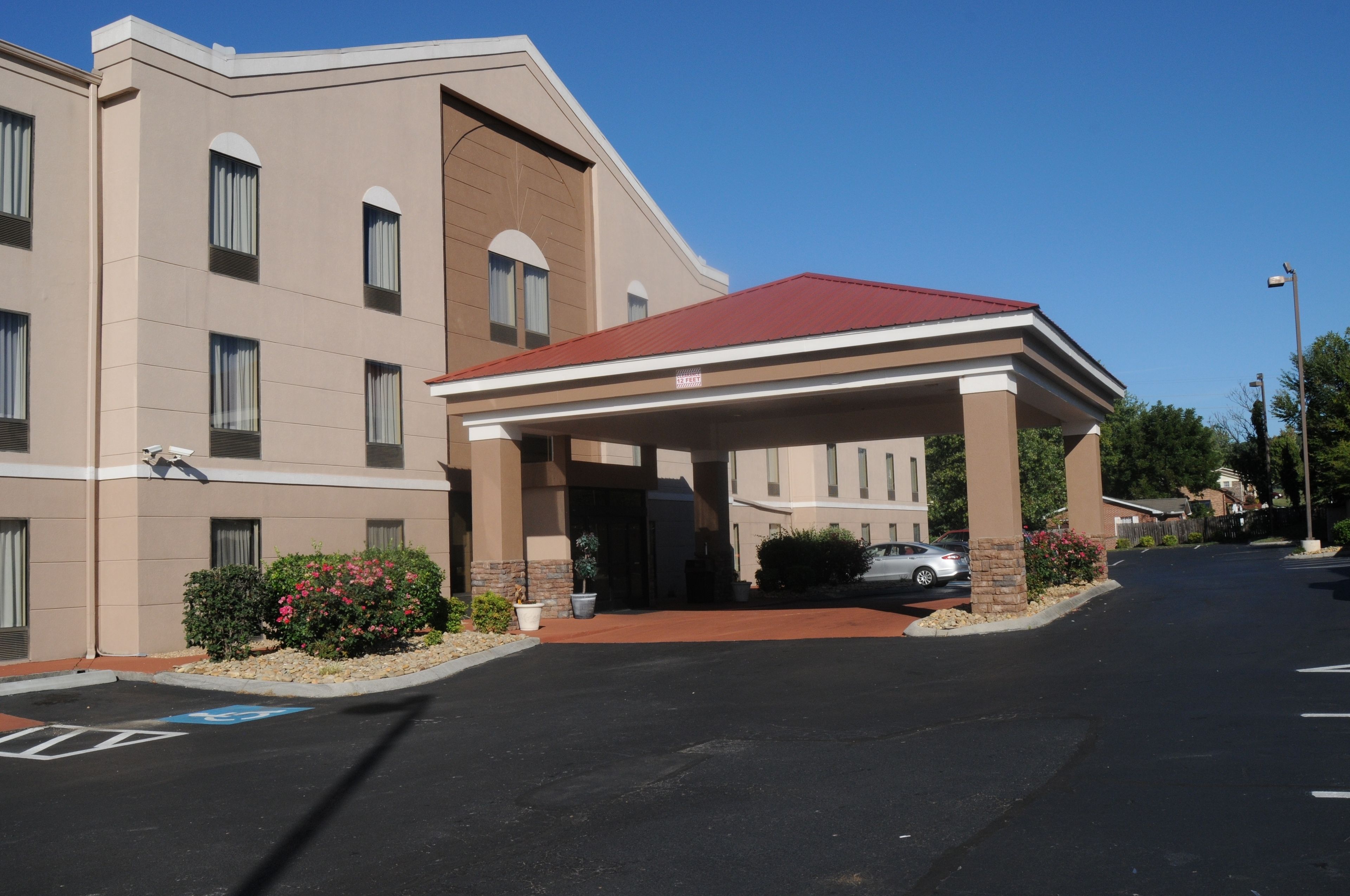 A hotel entrance with a covered walkway, a parking lot, and a clear blue sky.