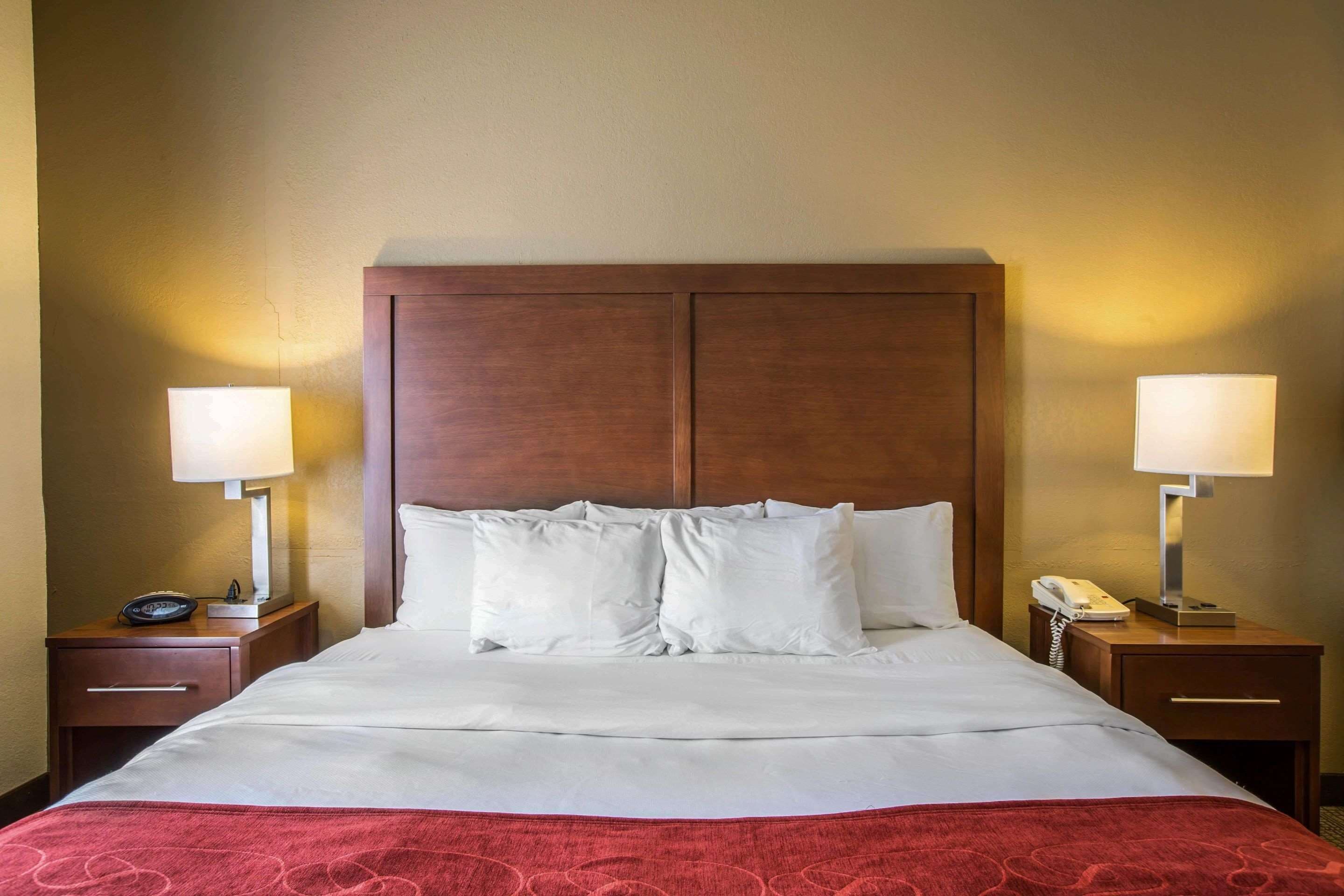 A hotel room with a large bed, two bedside tables with lamps, a telephone, and a drawer.