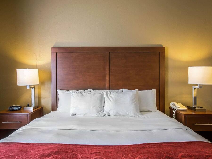 A hotel room with a large bed, two bedside tables with lamps, a telephone, and a drawer.