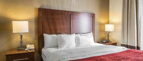A hotel room with a large bed, two bedside tables with lamps, a wooden headboard, and a red patterned throw blanket.