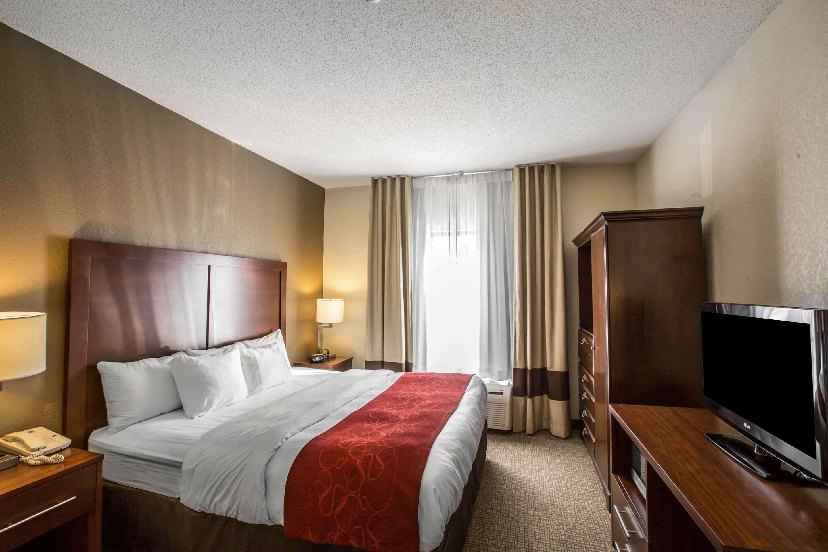Ein Hotelzimmer mit einem großen Bett, einem Fernseher, einem Schreibtisch mit Lampe und einem Kleiderschrank.