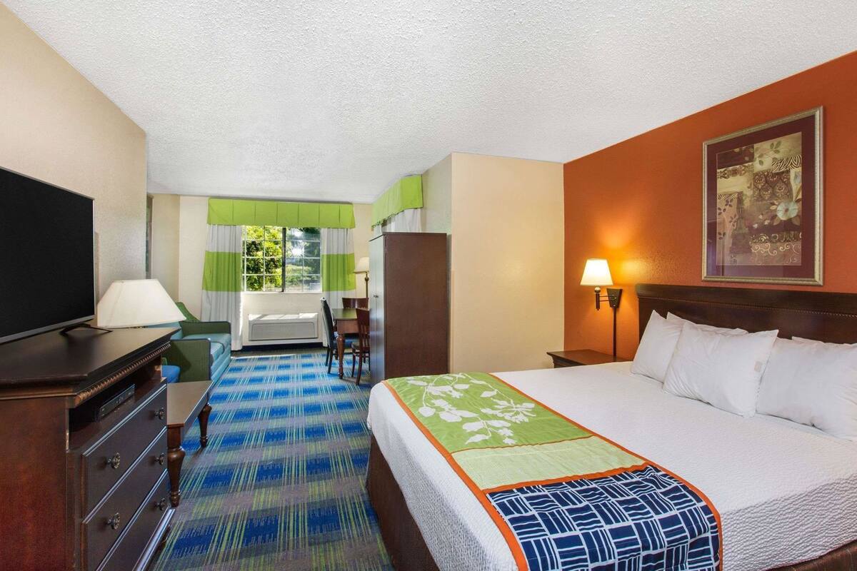 A hotel room with a bed, a TV, a desk, a chair, a lamp, and a painting on the wall.