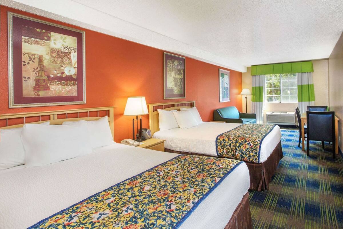 A hotel room with two beds, a desk, a chair, and a window with curtains.