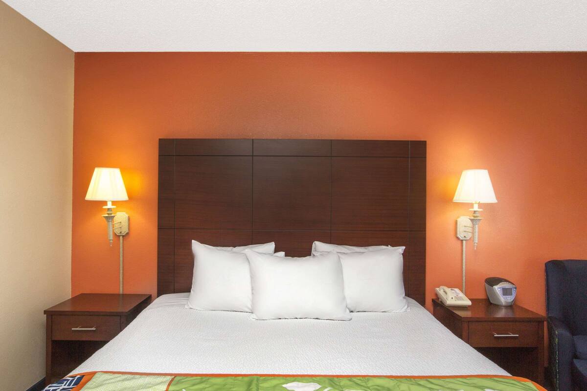 A hotel room with a large bed, two bedside tables, a nightstand, a chair, and a wall-mounted telephone.