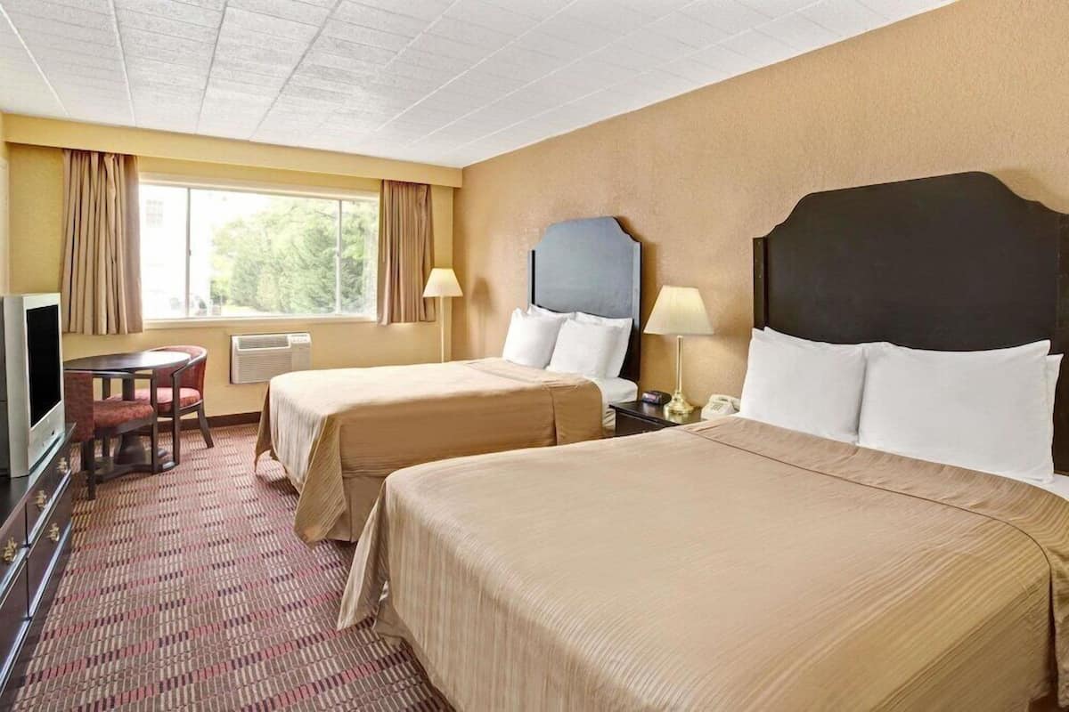 A hotel room with two beds, a desk, a TV, and a window with curtains.