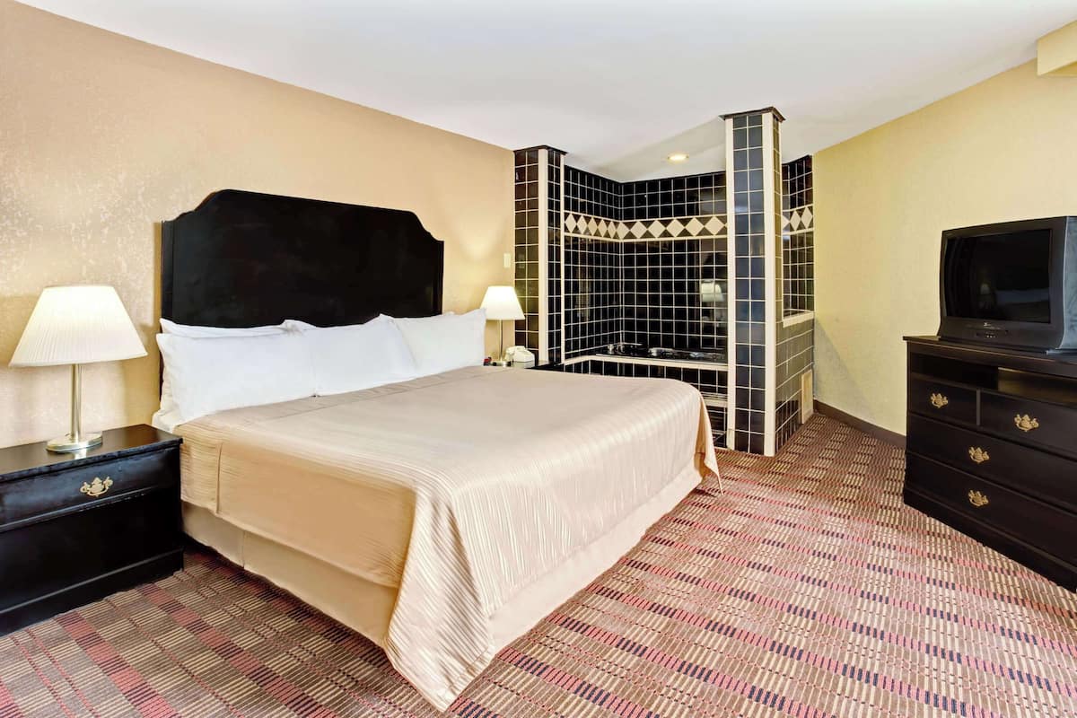 A hotel room with a large bed, two bedside tables with lamps, a TV, and a decorative wall unit.