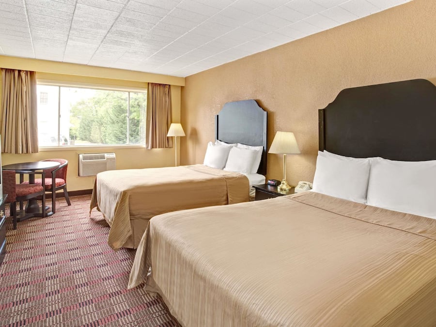 Une chambre d’hôtel avec deux lits, un bureau, une télévision et une fenêtre avec des rideaux.