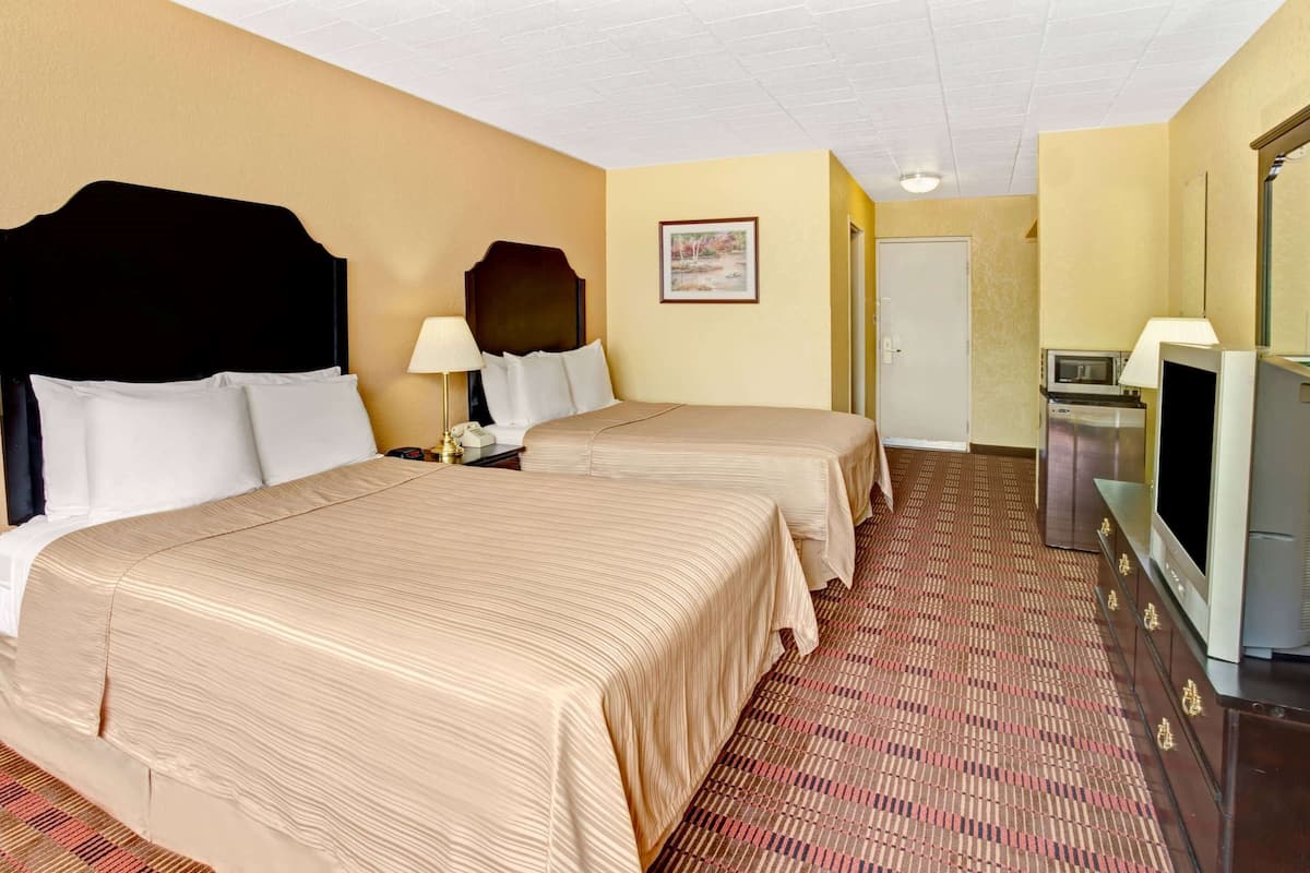 A hotel room with two beds, a television, a microwave, and a door.