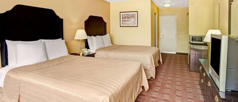 A hotel room with two beds, a television, a microwave, and a door.