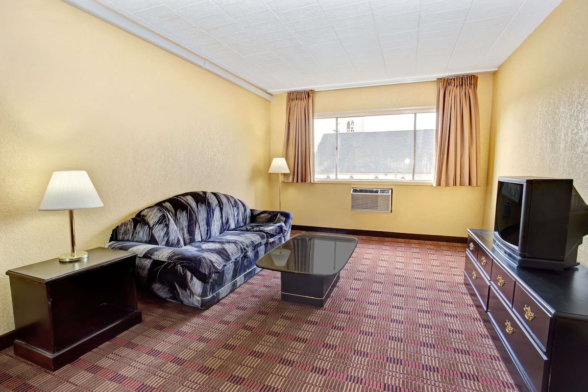 A hotel room with a sofa, a coffee table, a TV, a lamp, and a window with curtains.