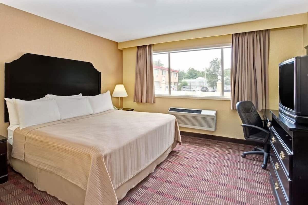 A hotel room with a bed, a desk with a computer, a chair, a television, and a window with curtains.