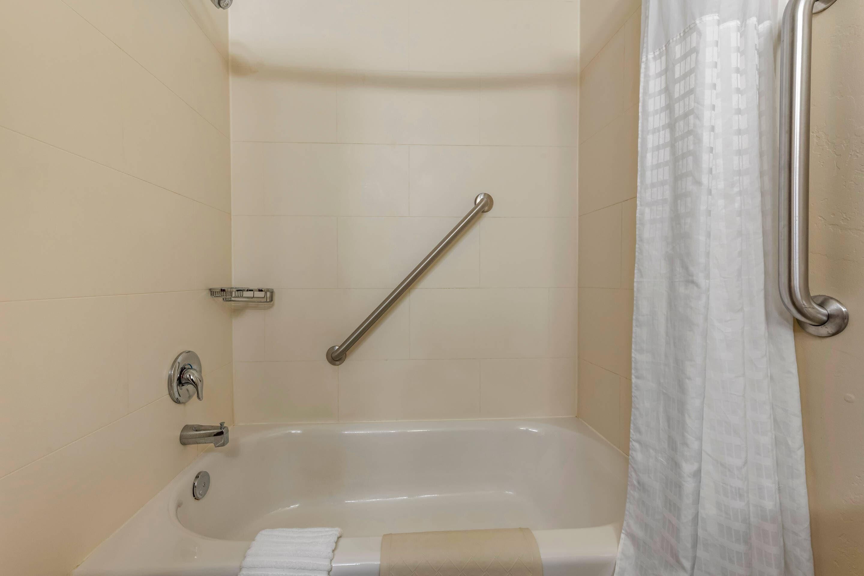 Un baño con bañera, barra de apoyo y cortina de ducha.