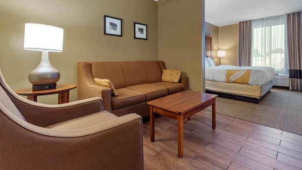 A hotel room with a bed, a sofa, a coffee table, a lamp, and two framed pictures on the wall.