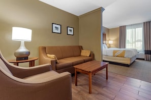 A hotel room with a bed, a sofa, a coffee table, a lamp, and two framed pictures on the wall.