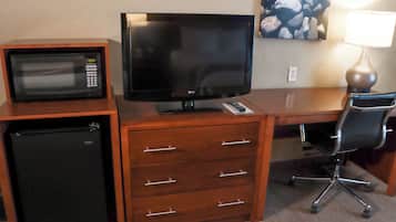 A compact kitchenette with a microwave, refrigerator, and a flat-screen TV on a wooden desk.