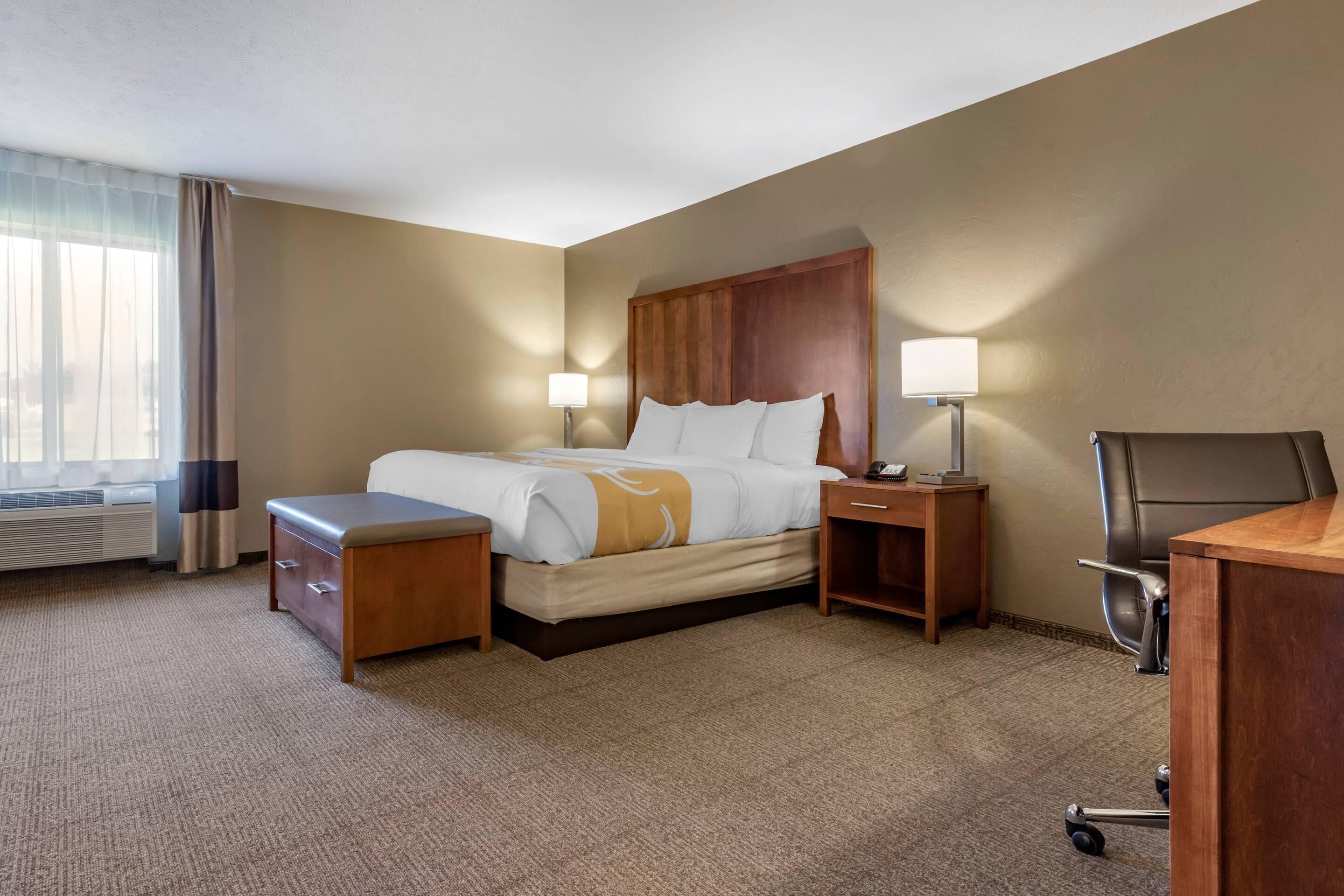 Una habitación de hotel con una cama, mesitas de noche, un escritorio, una silla y una ventana con cortinas.