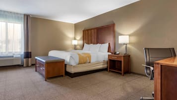 Una habitación de hotel con una cama, mesitas de noche, un escritorio, una silla y una ventana con cortinas.