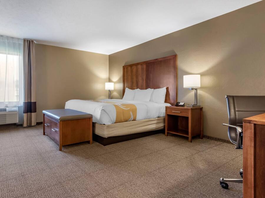 Una habitación de hotel con una cama, mesitas de noche, un escritorio, una silla y una ventana con cortinas.