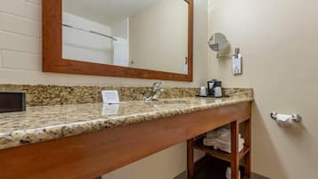 Un baño con encimera de granito, tocador de madera, un espejo grande, un perchero y un estante con toallas dobladas.