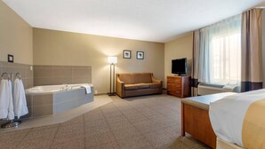 A hotel room with a large bed, a sofa, a TV, a desk, a lamp, a bathtub, and a window with curtains.