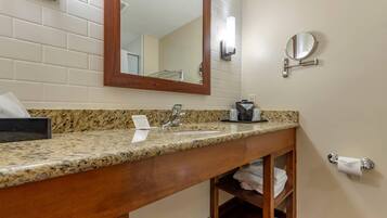 A bathroom with a granite countertop, a wooden vanity, a sink, a mirror, a towel rack, and a toilet paper holder.