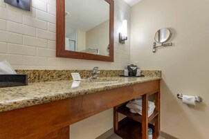 Un baño con encimera de granito, tocador de madera, lavamanos, espejo, toallero y soporte para papel higiénico.