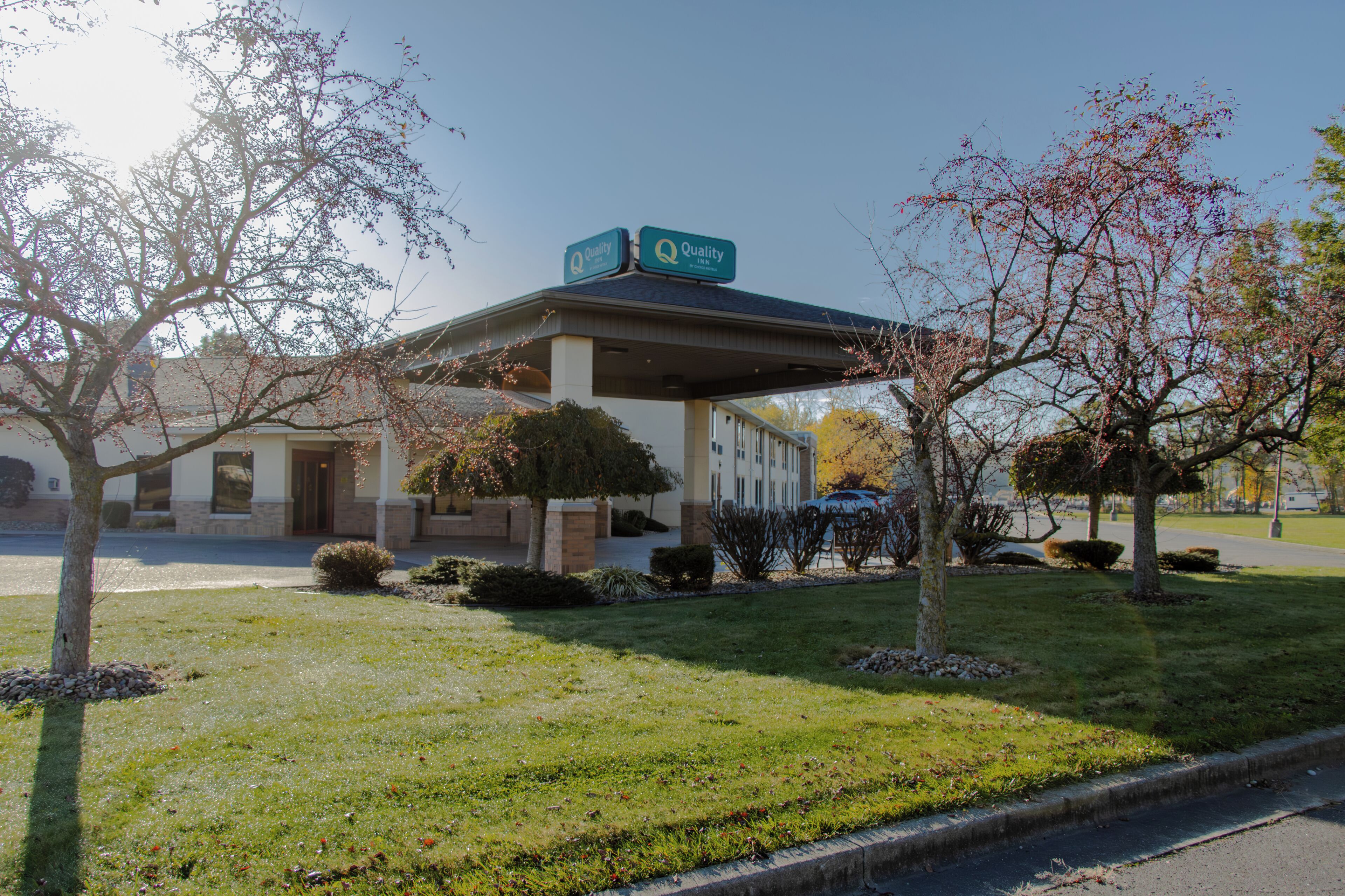 A building with a covered outdoor area, a sign indicating 'Quality,' and a parking lot with a few cars.