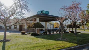 A building with a covered outdoor area, a sign indicating 'Quality,' and a parking lot with a few cars.