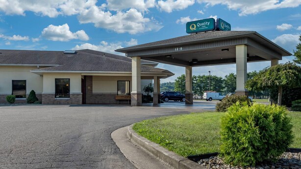 A hotel with a covered parking area, a sign indicating 'Quality Inn,' and a clear blue sky with clouds.