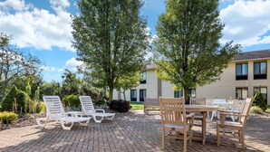 A patio area with lounge chairs and a table, surrounded by trees and a building in the background.