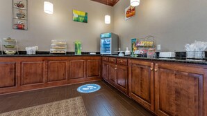 A hotel lobby with a wooden reception desk, a refrigerator, a coffee station, and a patterned rug.