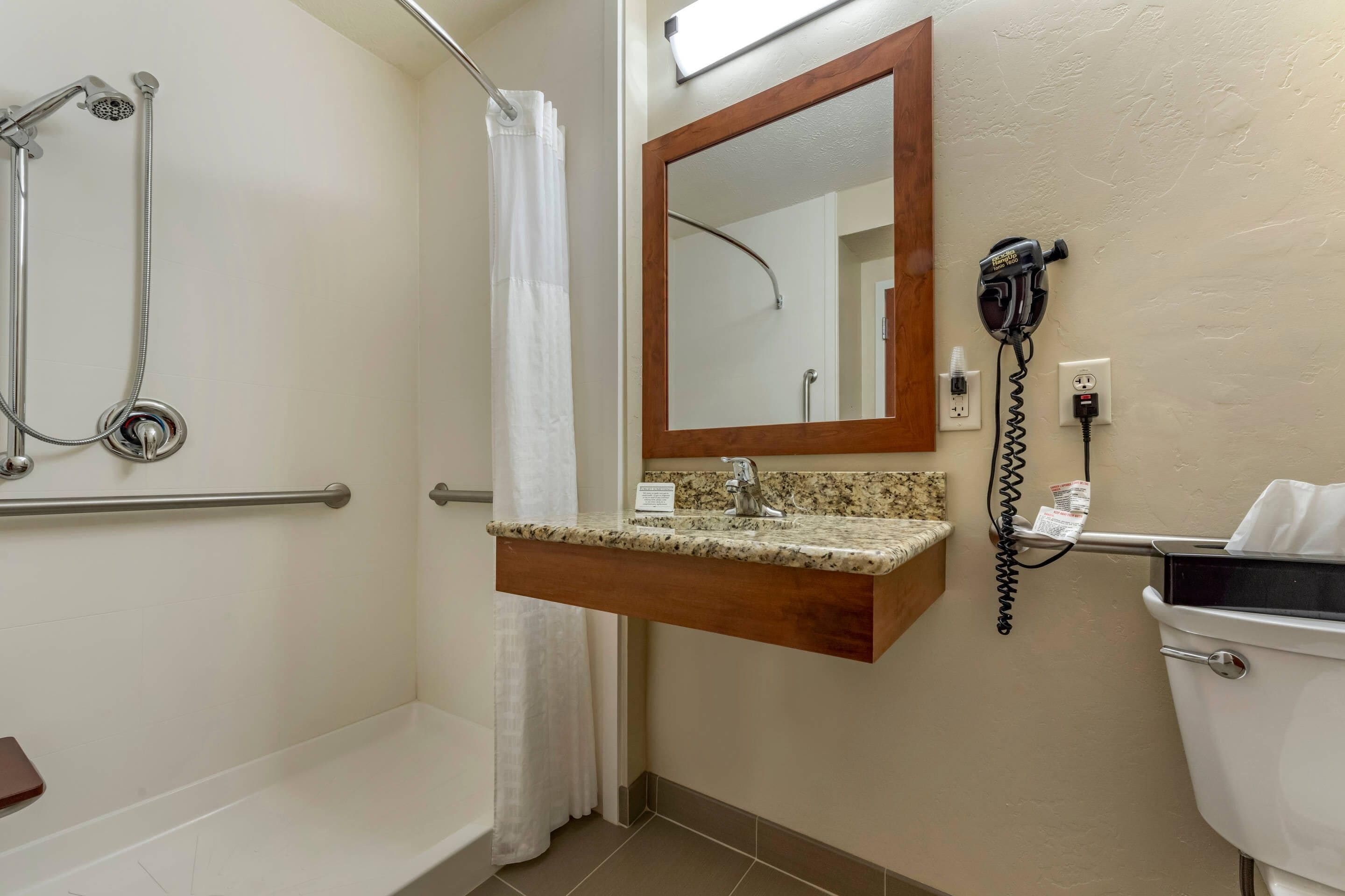 A bathroom with a shower, a toilet, a sink with a mirror, and a hairdryer on the wall.