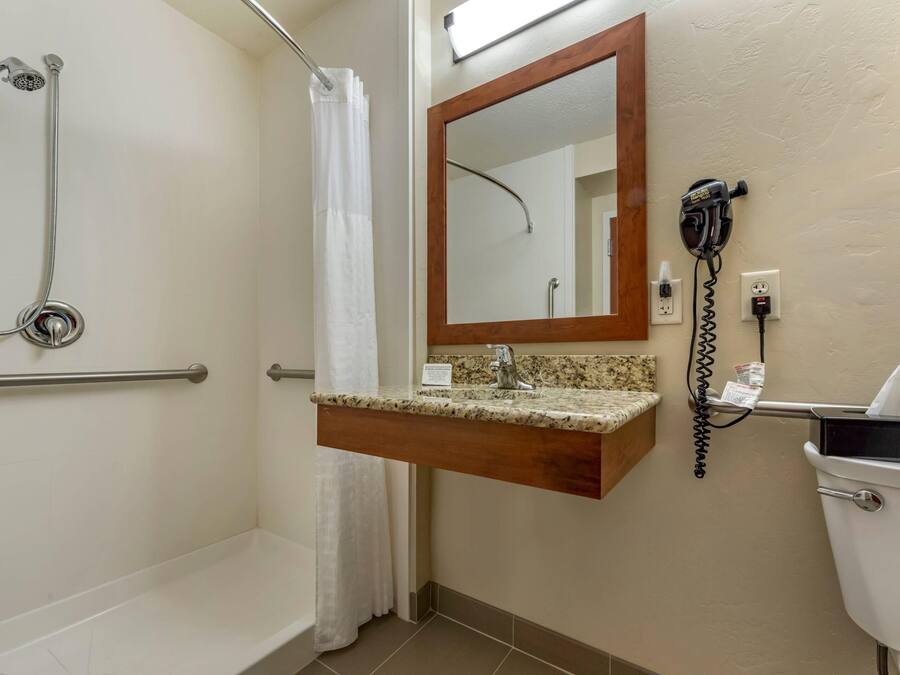 A bathroom with a shower, a toilet, a sink with a mirror, and a hairdryer on the wall.