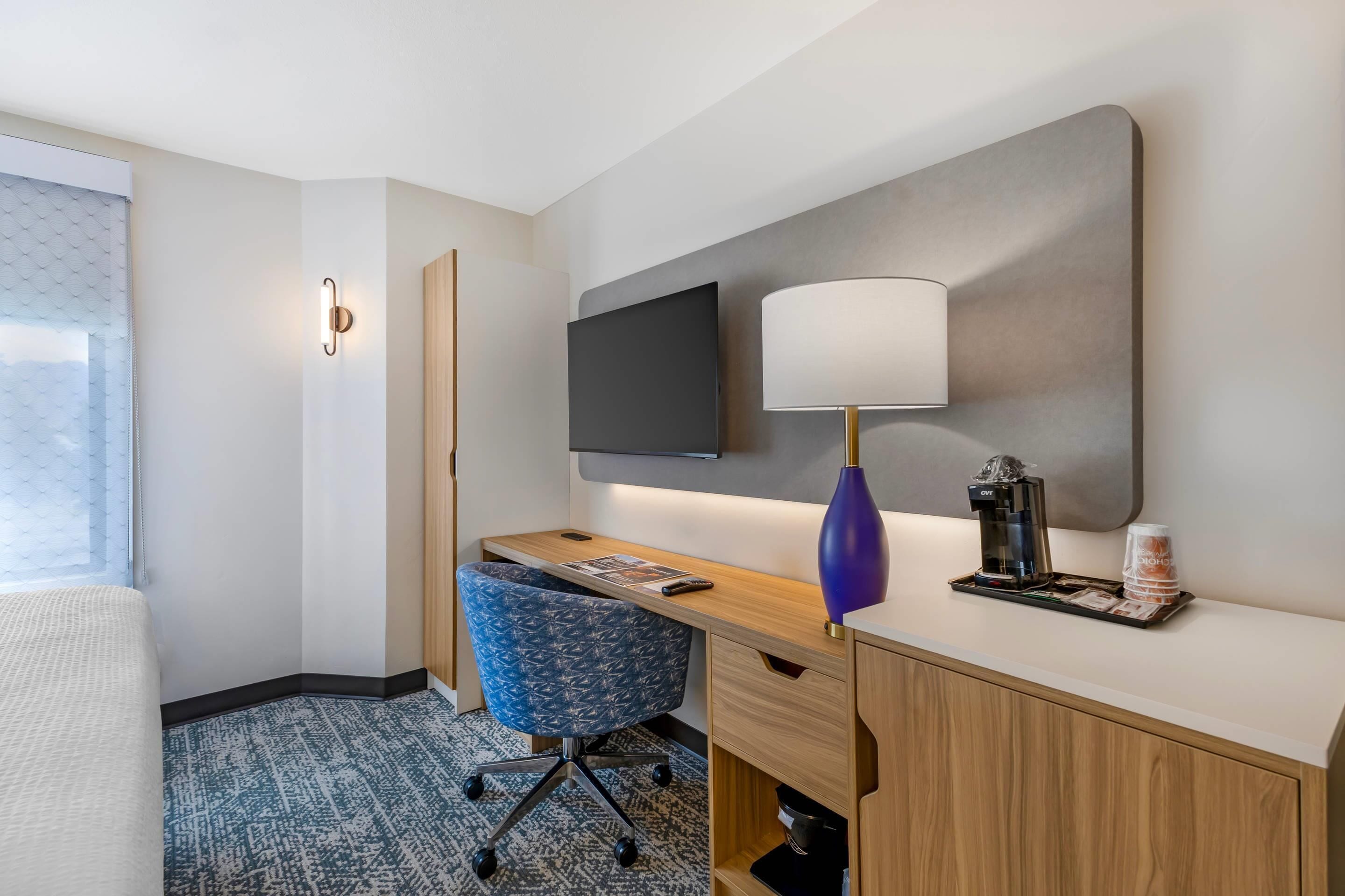 Una habitación de hotel con escritorio, silla, televisor, lámpara, cafetera y cama.