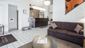 A modern hotel room with a sofa, a coffee table, a kitchen area, and a large painting on the wall. - Sleep Inn South Jordan - Sandy (South Jordan)