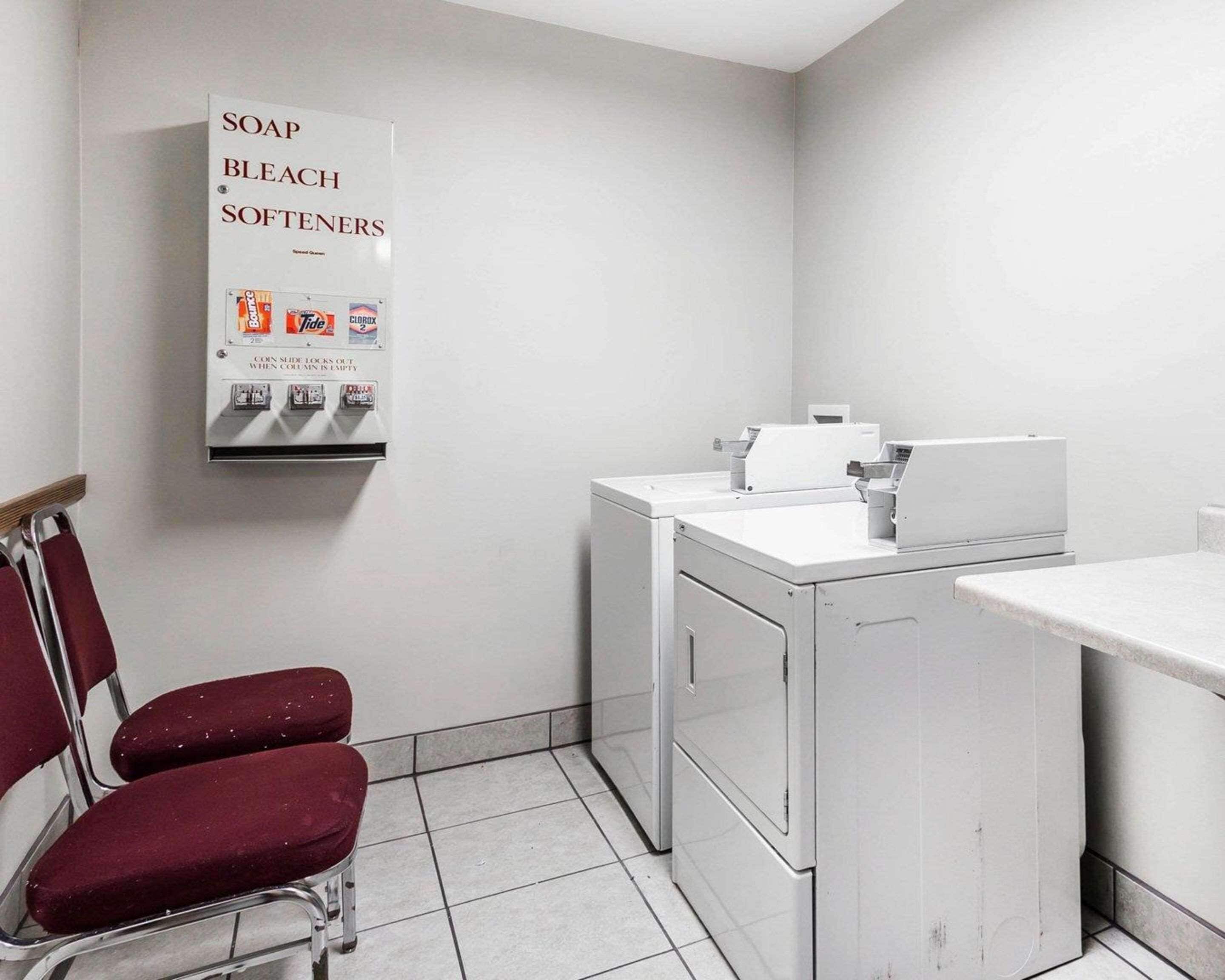 Un espace buanderie comprenant un distributeur de savon et d’eau de Javel fixé au mur, deux chaises rouges et un lave-linge.