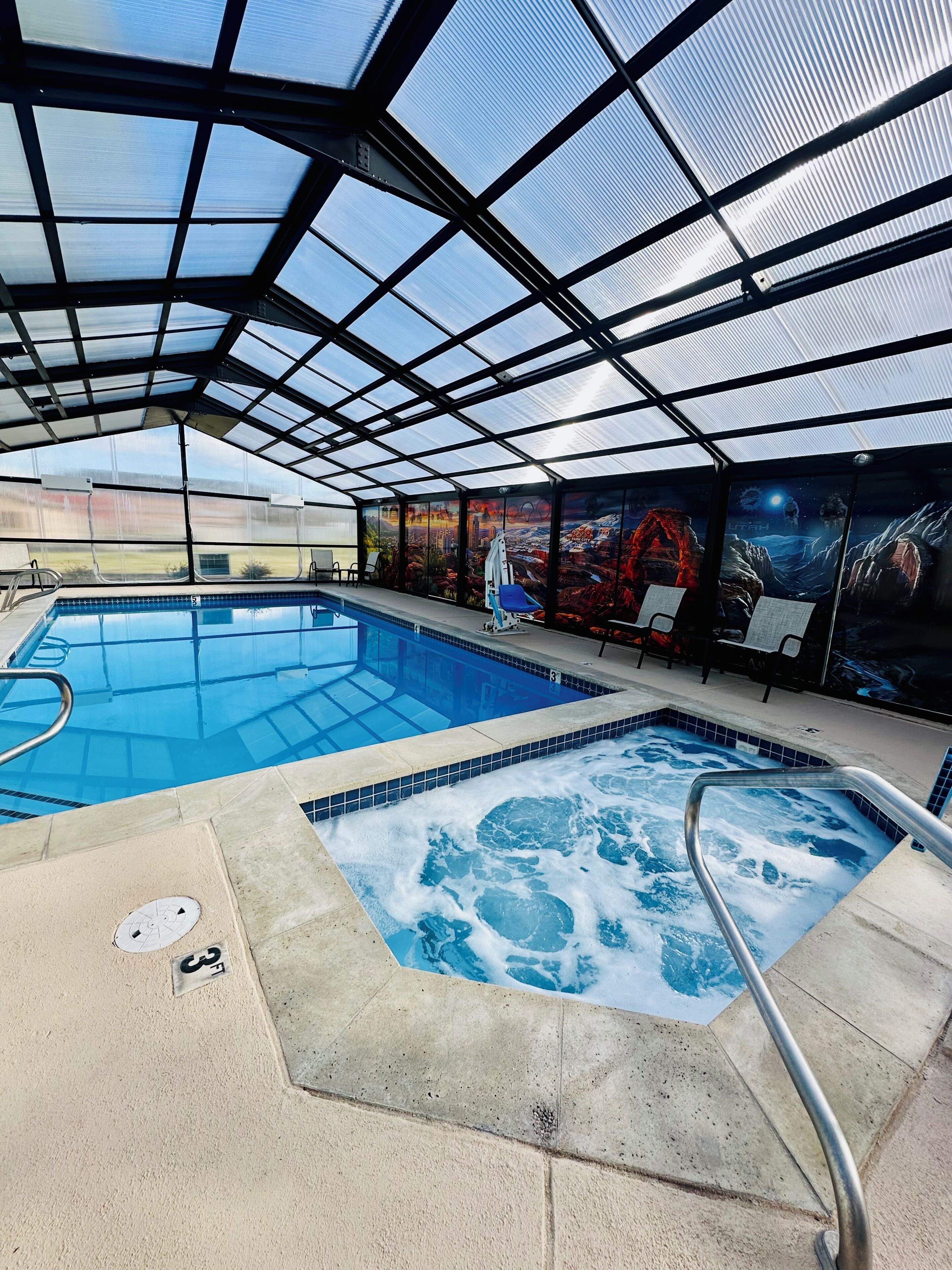 A covered swimming pool with a hot tub, lounge chairs, and a mural on the wall.