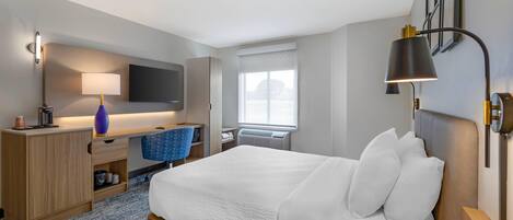 A hotel room with a bed, desk, chair, TV, lamp, and phone.