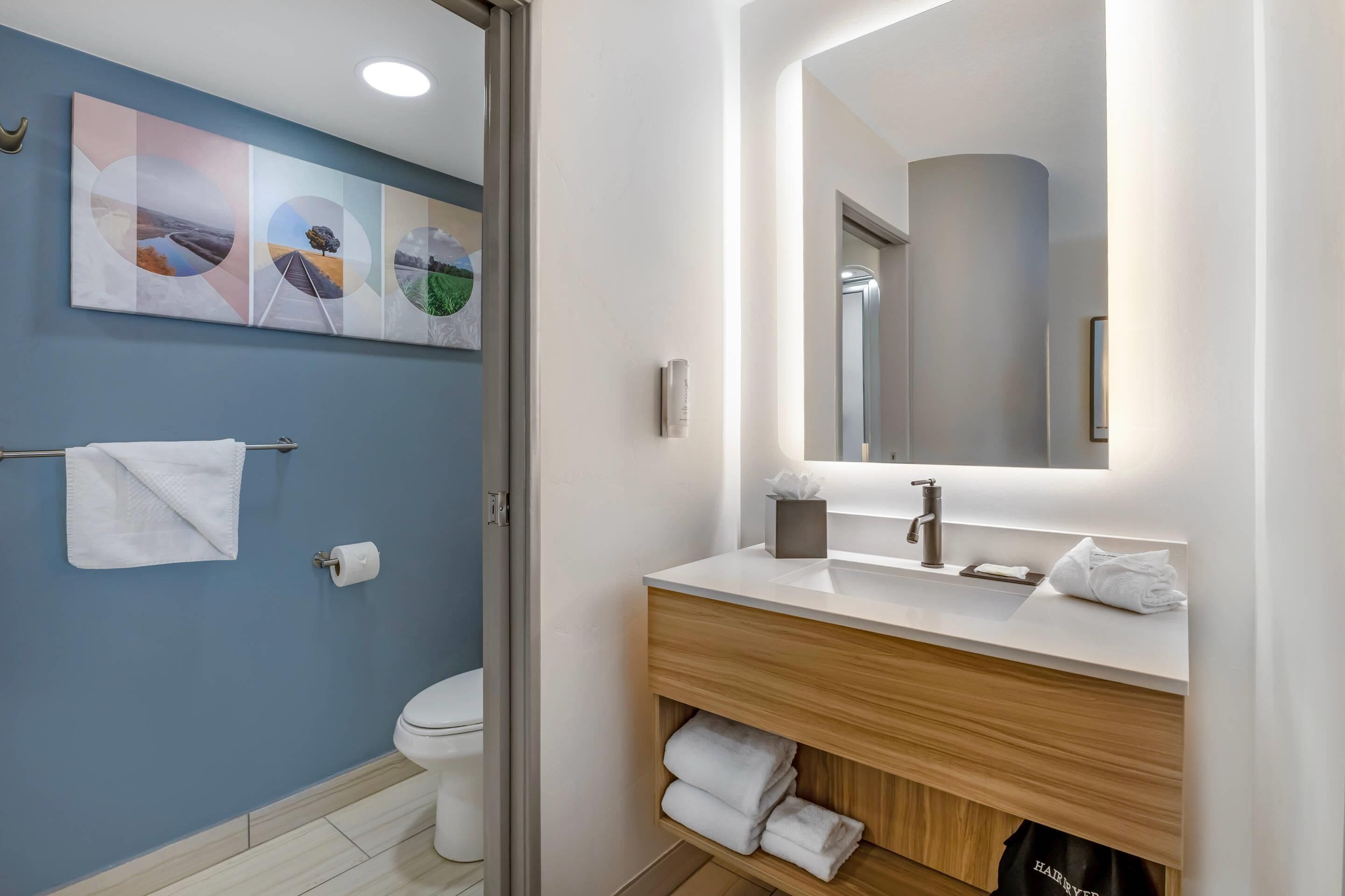 Uma casa de banho moderna com sanita, lavatório, espelho e porta-toalhas.
