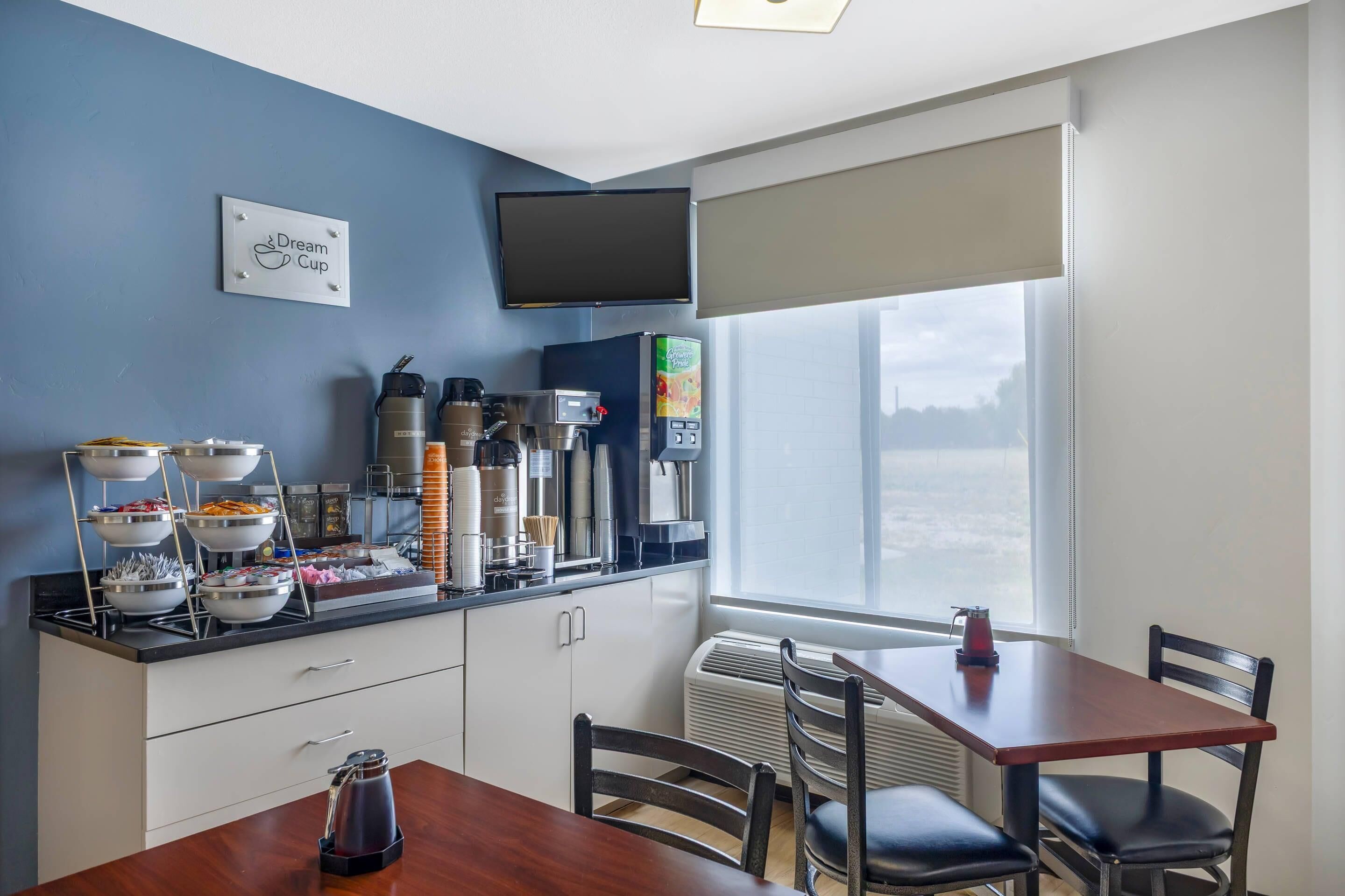 Une cuisine moderne dotée d’un coin café, d’un espace repas avec une table et des chaises, et d’une grande fenêtre offrant une vue sur la ville.