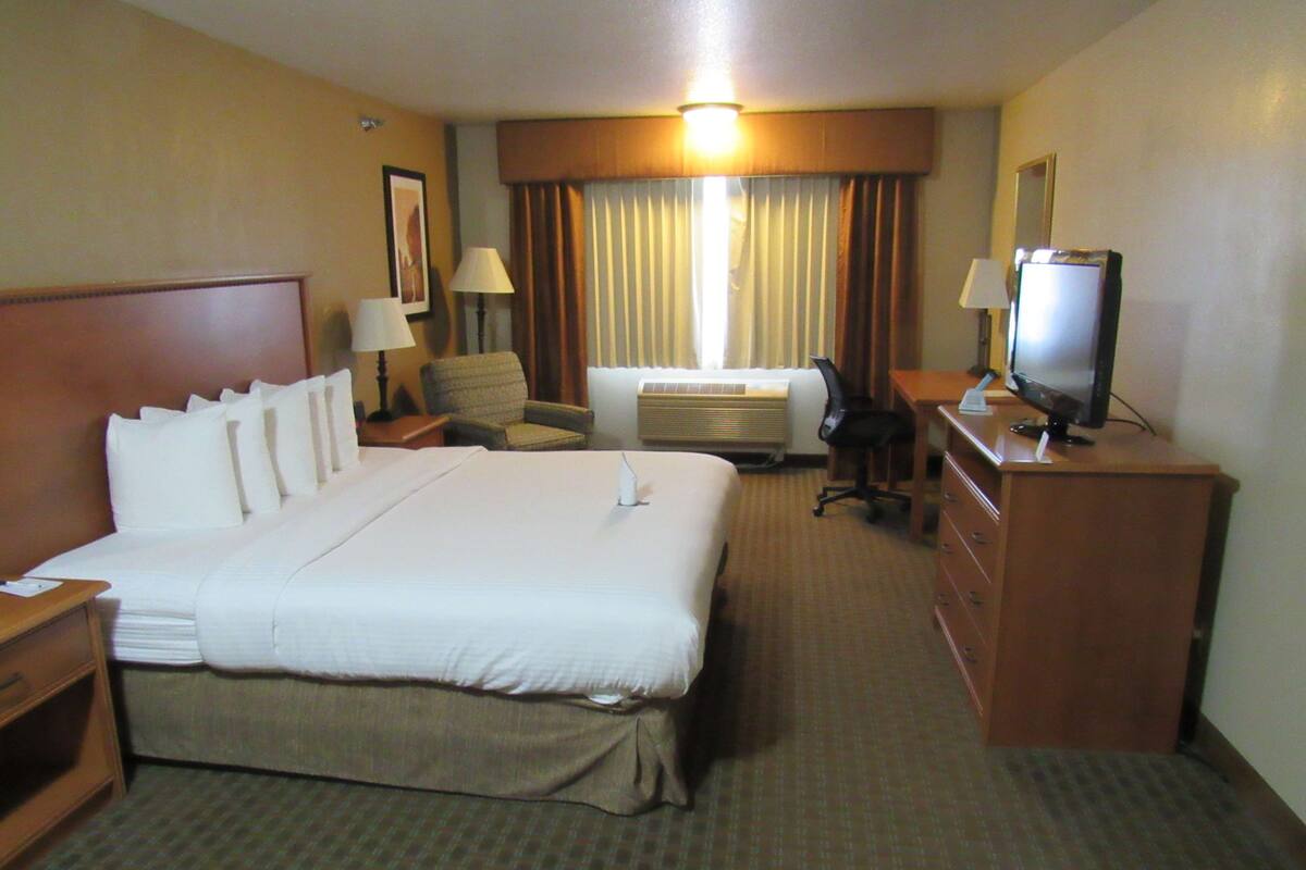 Une chambre d’hôtel avec un grand lit, un bureau avec une télévision, une chaise, un appareil de climatisation et une lampe.