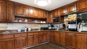 A kitchen with wooden cabinets, a microwave, a coffee maker, and a refrigerator. - Best Western Empire Towers (Sioux Falls)