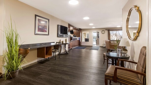 A modern hotel lobby with a wooden floor, a reception desk, a dining area with chairs and a table, a large mirror, and a clock on the wall. - Best Western Empire Towers (Sioux Falls)